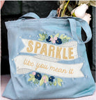 Blue tote bag with 'Sparkle like you mean it' text and floral design.