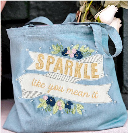 Blue tote bag with 'Sparkle like you mean it' text and floral design.